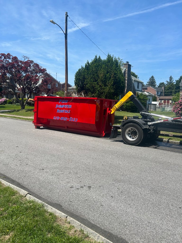 Penn Dumpster Rentals truck dropping off a red roll-off dumpster on a residential street